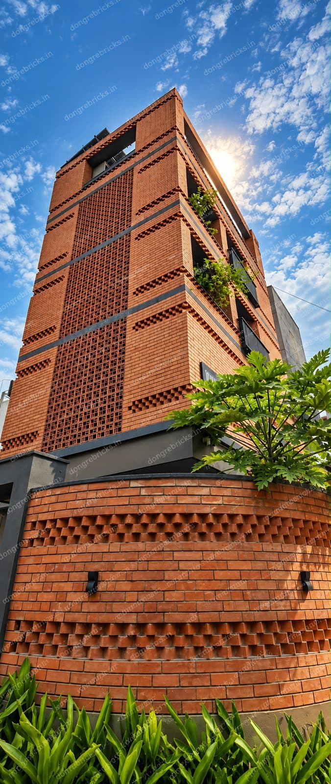 Multi-storey exposed brick facade with perforated jali panels and a curved dogtooth boundary wall